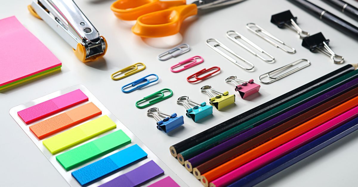 An assortment of colorful paperclips, sticky notes, and colored pencils neatly arranged on a white surface.