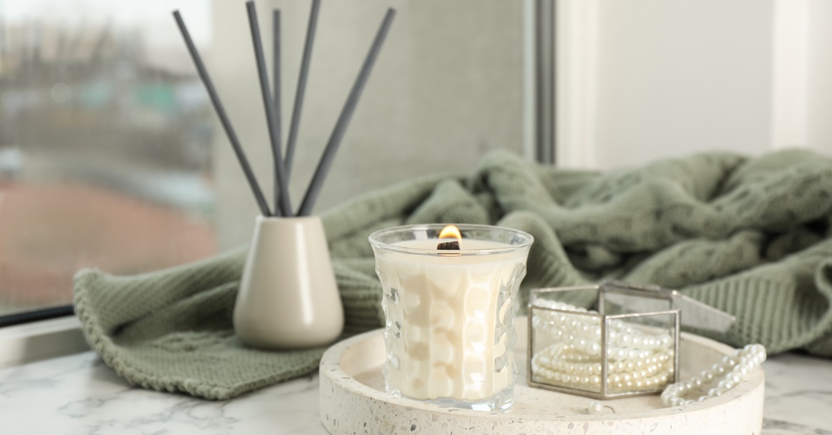 A close-up of a small, white tray on a dresser holding a glass jar with jewelry and a white burning candle.