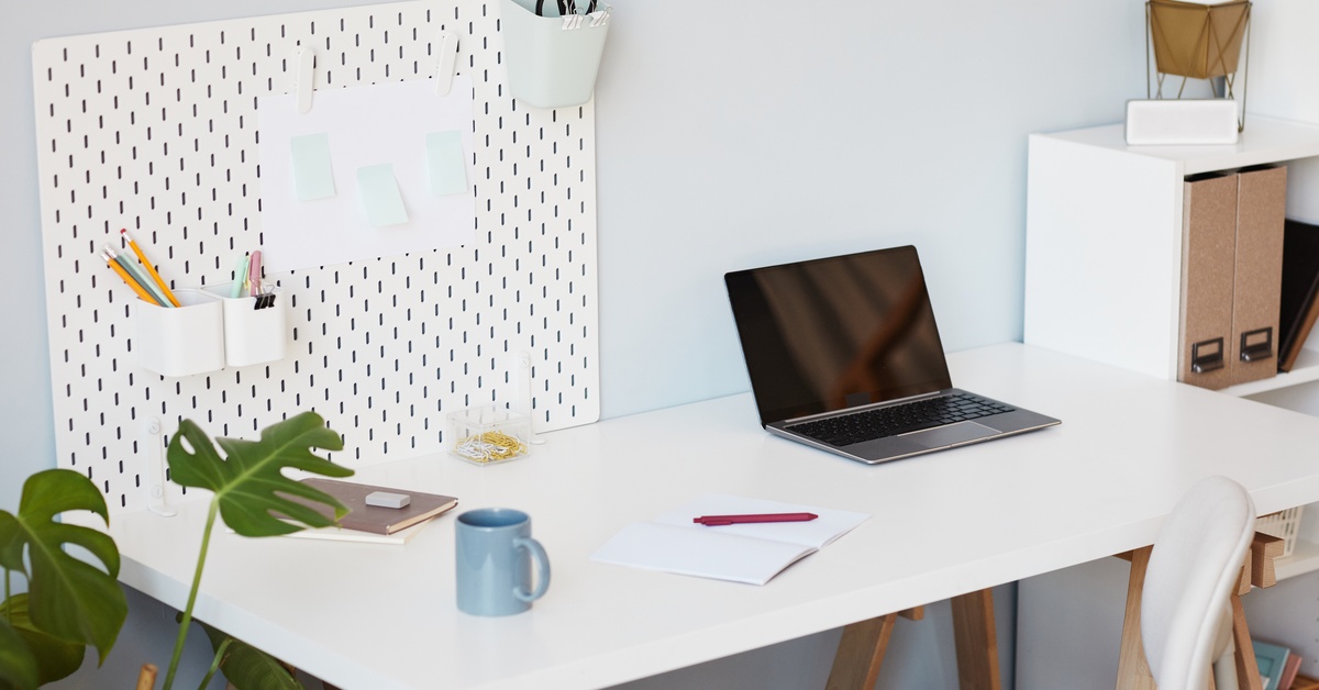 A well-organized and clean desk on a wall with a pegboard and pencil cups attached. A laptop sits open on the desk.