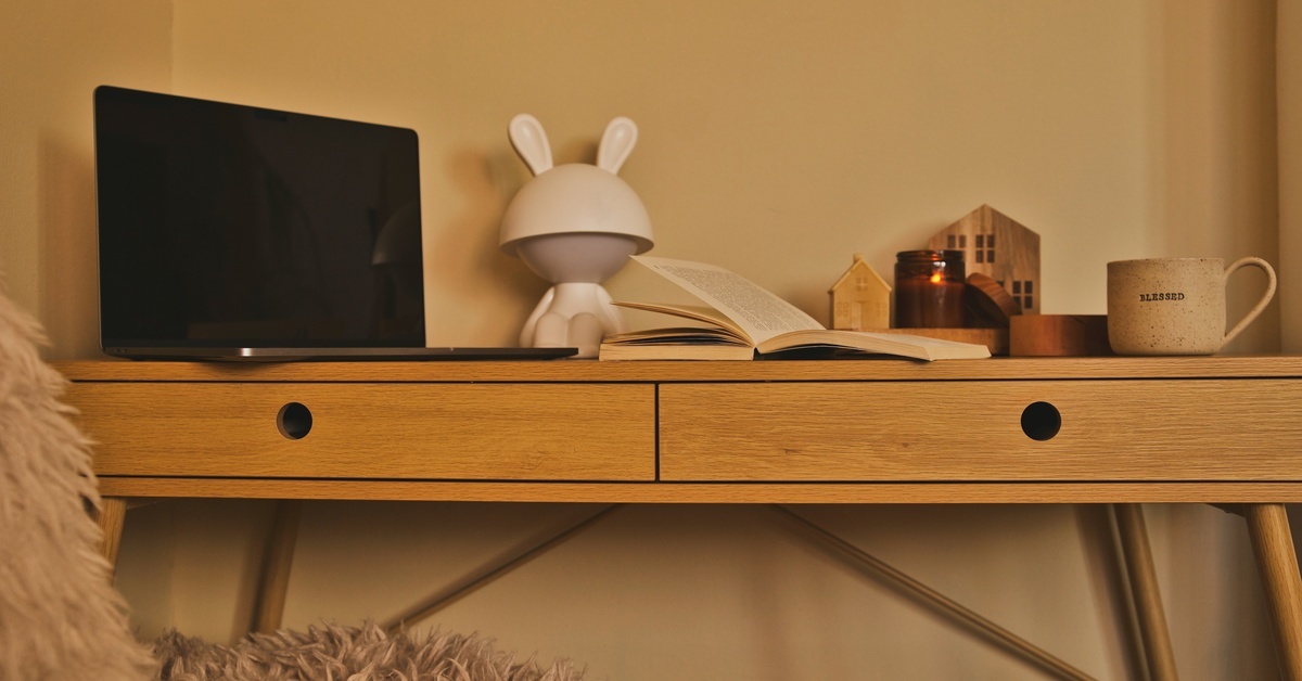A cozy and warm-colored home office setup with a black laptop, open book, candle, small figure, and a mug. A cozy and warm-colored home office setup with a black laptop, open book, candle, small figure, and a mug.