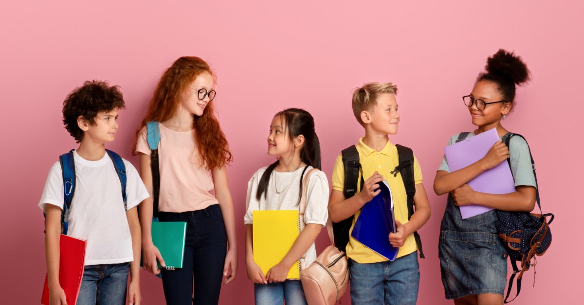 5 Creative Tiny Prize Ideas for Classroom Rewards A group of kids of different age ranges and genders holding schoolbooks against a pink wall background.