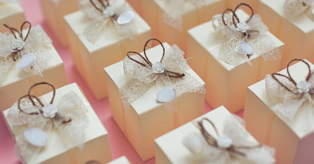 A close-up of rows of tiny boxes with lace ribbons sitting on a table. The boxes are beige in color.
