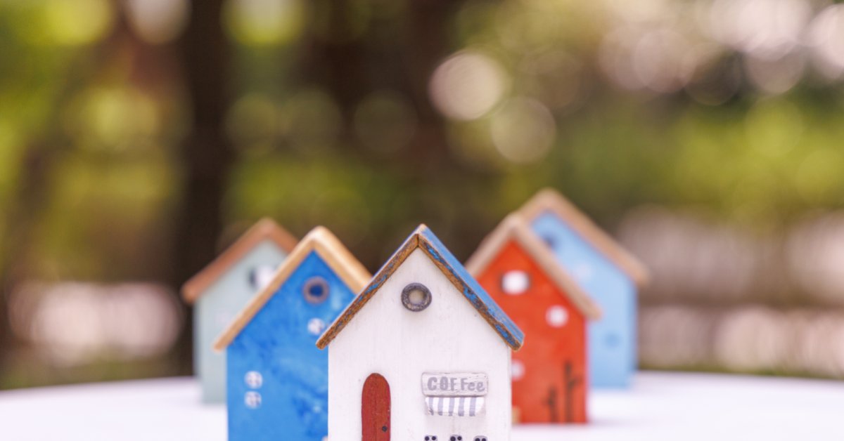 Tiny Architecture Models for Creative Adults Miniature wooden houses in white, blue, pink, and yellow arranged on a white surface with green blur behind them.